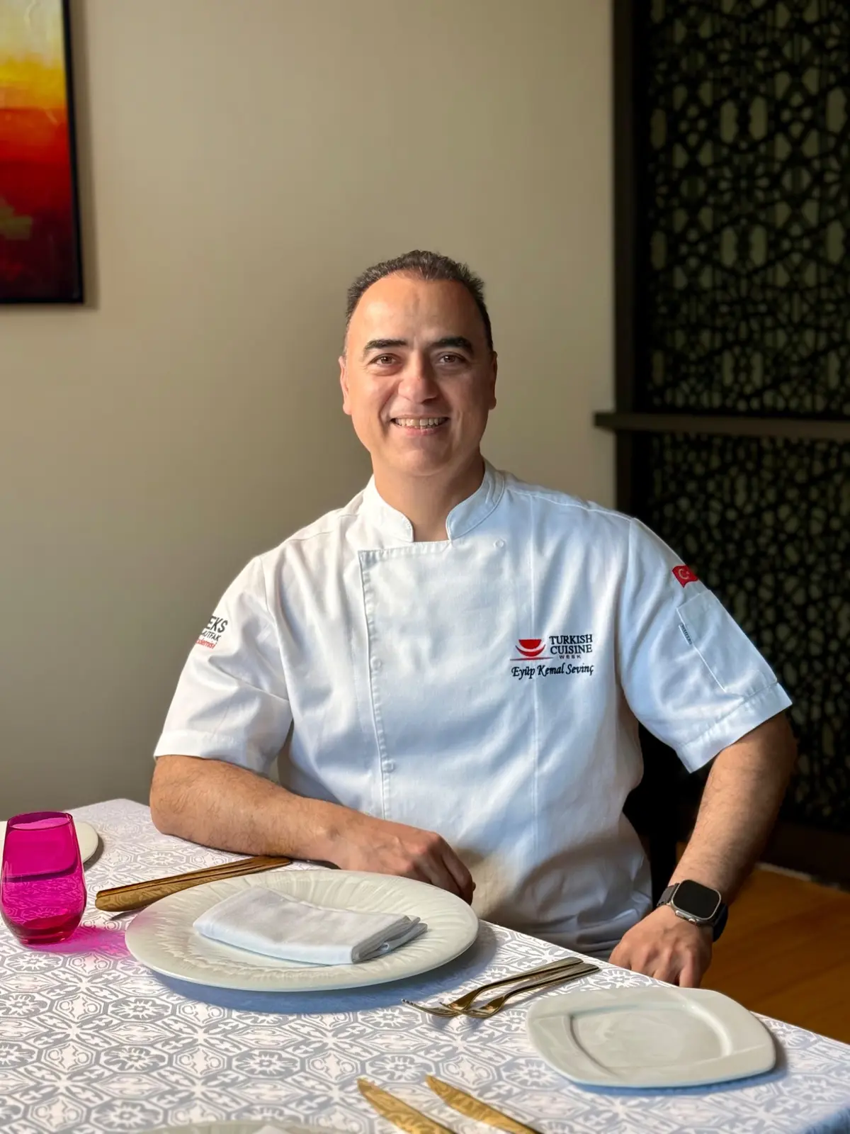 Eyüp Kemal Sevinç, beyaz şef ceketiyle bir restoran masasında